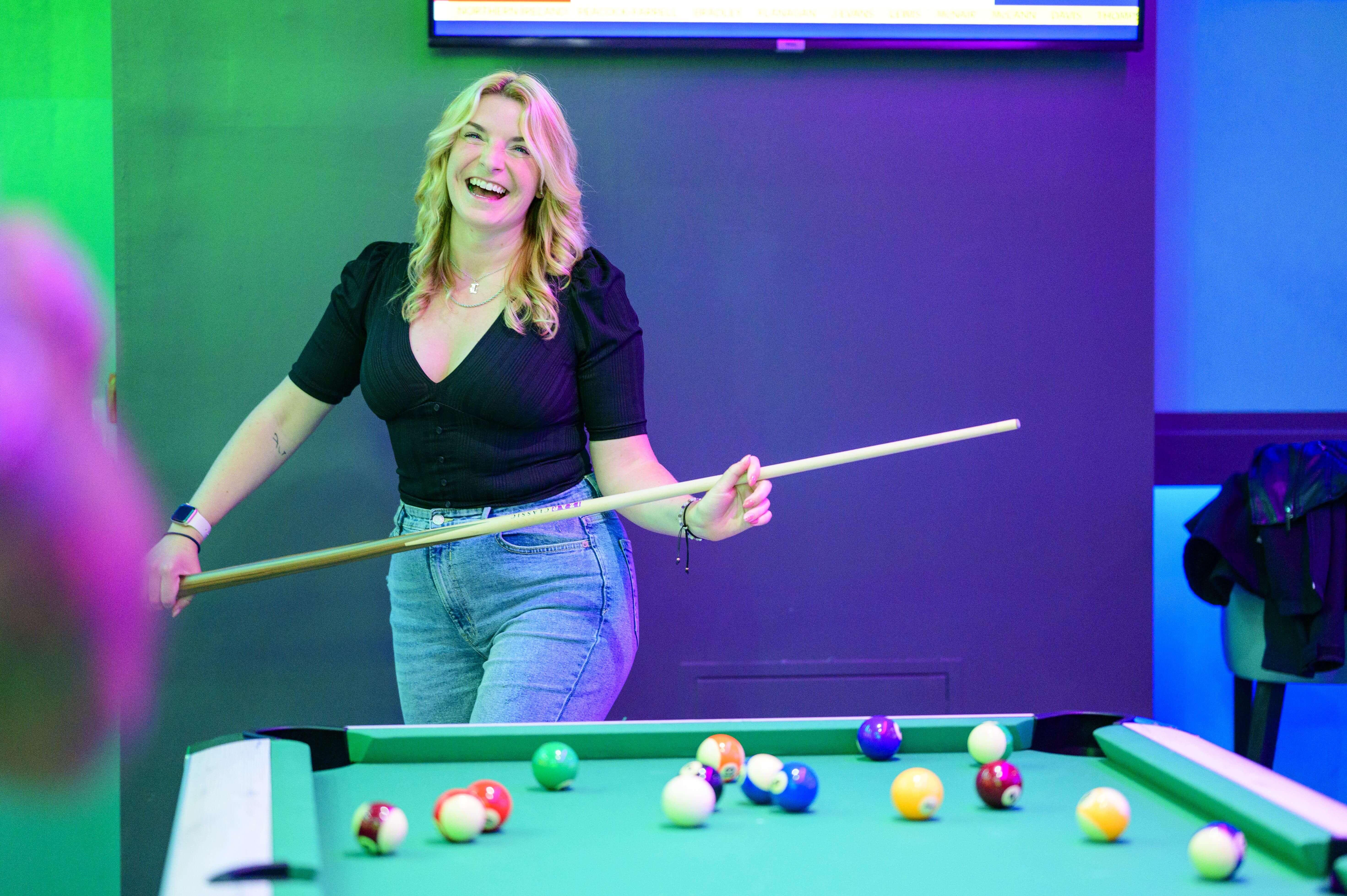 Young Woman Holding Cue In Front Of Pool Table