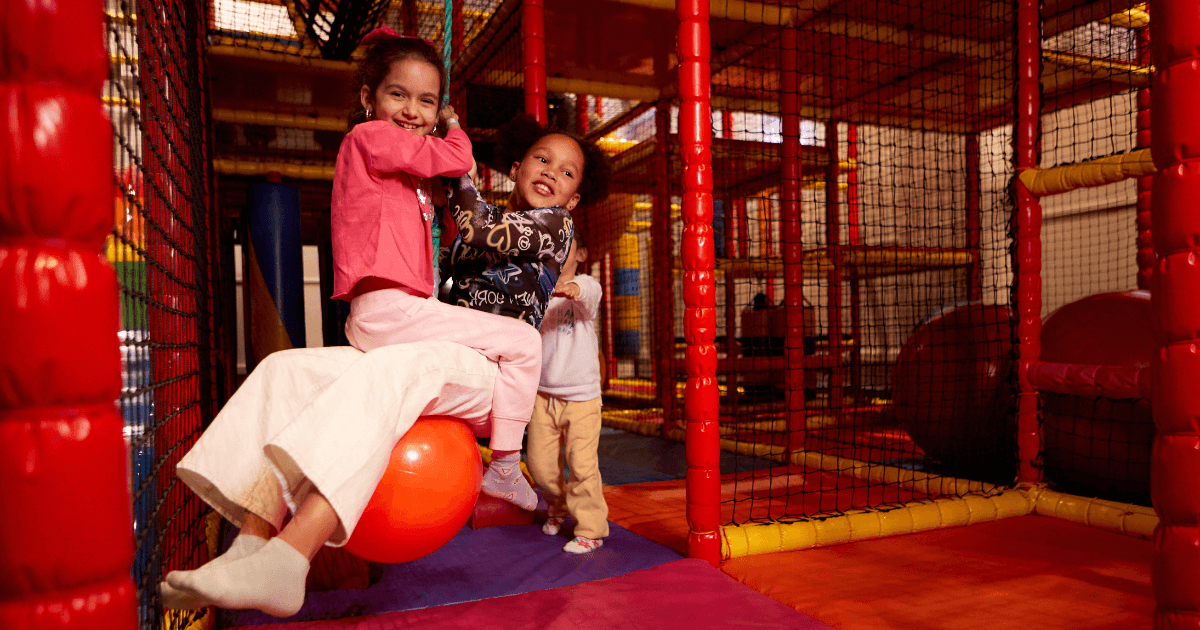 Two Young Girls Swinging On A Ball In The Soft Play Area (1)