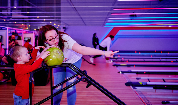 Mum helping toddler boy use bumpers to bowl