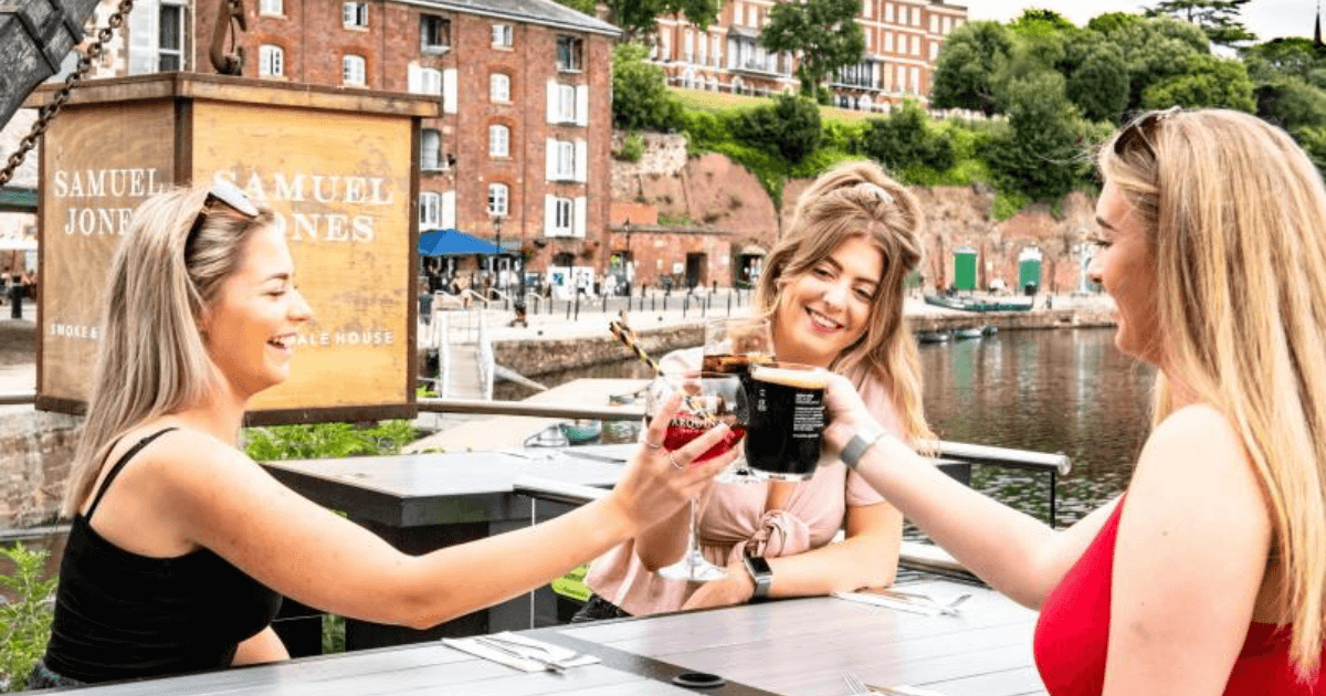 Three Girls Enjoying A Drink By The River In Exeter