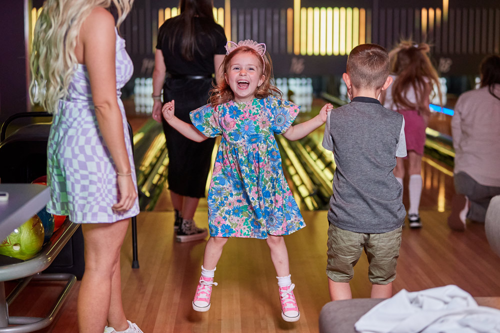 Excited young girl bowling on family day out
