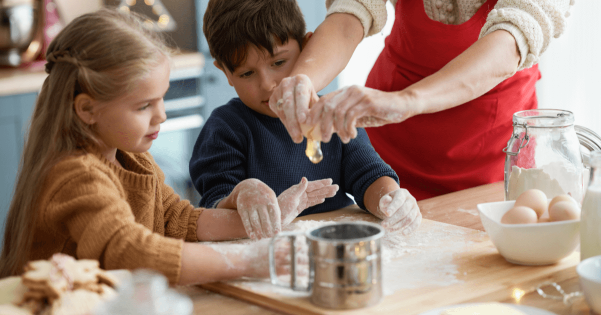 A Family In The Kitchen With Woman Breaking Egg Onto The Table (1)