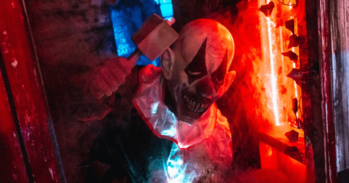 Scary Clown Holding Mallet Behind Glass In An Escape Room (1)